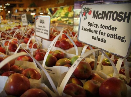 Baskets of McIntosh and Gala apples displayed in a market, with signs describing their qualities.