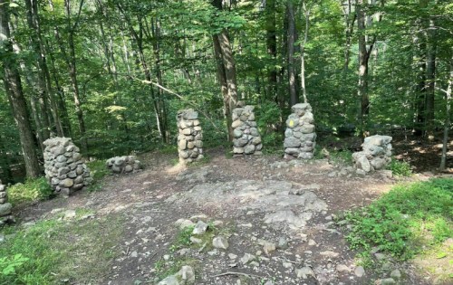 Stone pillars stand in a clearing surrounded by lush green trees in a forested area.