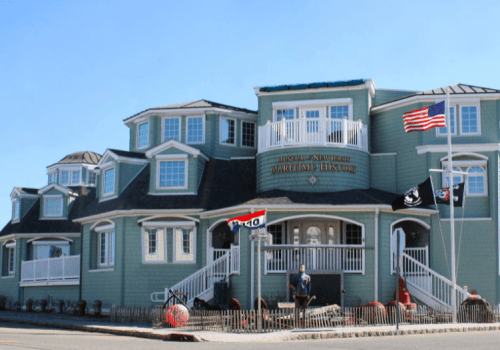 A large, light blue building with multiple gables, flags, and a porch, likely a museum or historical site.