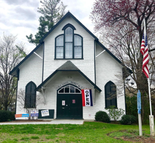 A white, historic building with large windows, an "OPEN" sign, and an American flag in front.