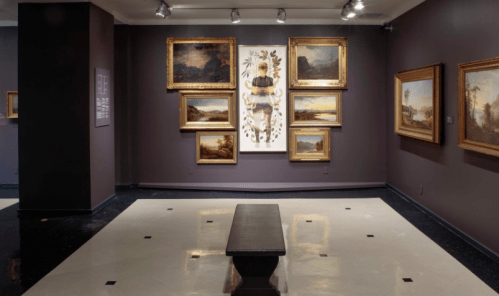 Art gallery interior featuring framed paintings on dark walls and a central bench on a polished floor.