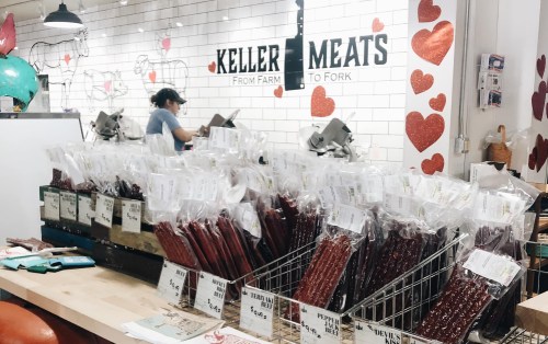 A display of packaged meats at Keller Meats, with a worker in the background and heart decorations on the wall.
