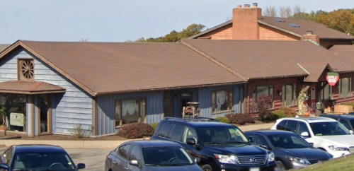 A rustic building with a blue and brown exterior, surrounded by parked cars and trees in the background.