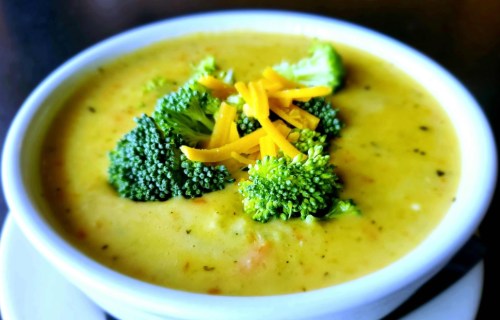 A bowl of creamy broccoli soup topped with fresh broccoli florets and shredded cheese.