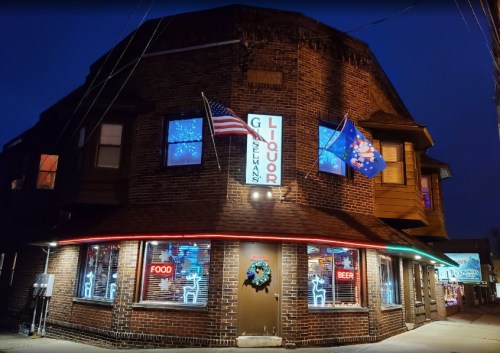 A brick building at night with neon signs for food and beer, featuring flags and festive decorations.
