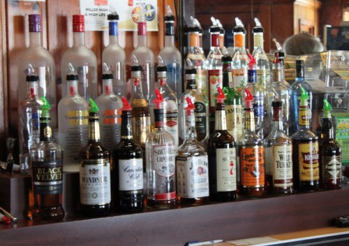 A bar shelf displaying various bottles of liquor, including whiskey, vodka, and rum, with colorful pour spouts.