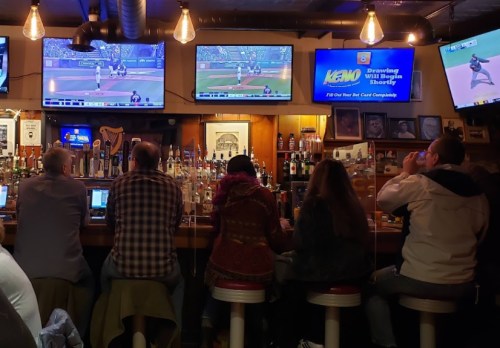A cozy bar scene with patrons watching baseball on multiple screens while seated at the counter.