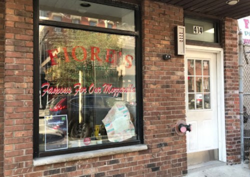 Exterior of Fiore's, a brick storefront with a large window displaying the name and a sign about their mozzarella.