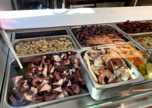 A display of seafood, including octopus, olives, and various marinated items in metal trays.