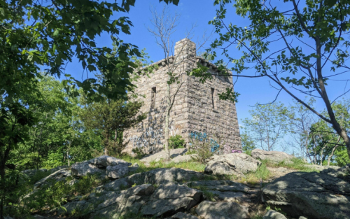 A stone tower surrounded by greenery and rocks under a clear blue sky.