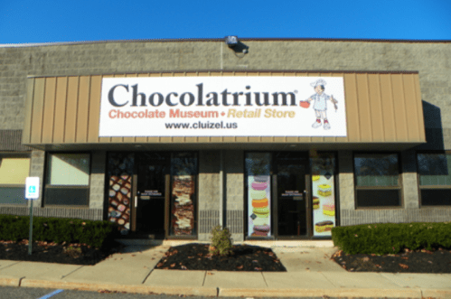 Exterior of the Chocolatrium, a chocolate museum and retail store, featuring a large sign and colorful window displays.