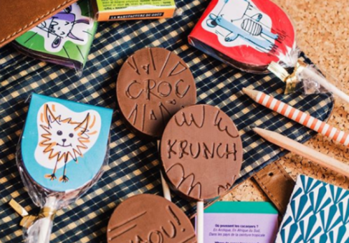 Colorful chocolate treats with playful designs and text, arranged on a textured surface with pencils and packaging.
