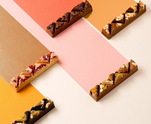 Colorful chocolate bars with various toppings arranged on a pastel background.