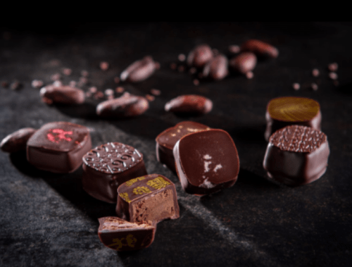 Assorted chocolate truffles with various designs, some whole and others partially bitten, on a dark surface.