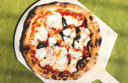 A freshly baked pizza with mozzarella, basil, and a golden crust on a wooden pizza peel.