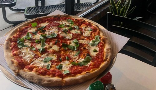 A large pizza topped with tomato sauce, mozzarella cheese, and fresh basil, served on a silver platter in a casual setting.