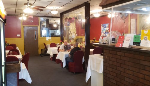 A cozy restaurant interior with red walls, white tablecloths, and two patrons seated at a table.