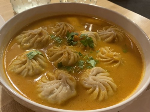 A bowl of soup with dumplings, garnished with cilantro, in a rich, orange broth.