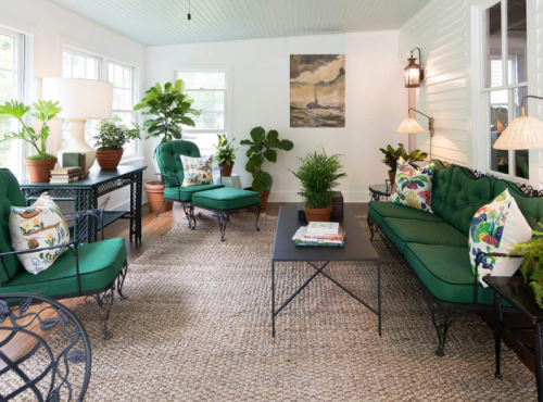 A bright, airy living room with green furniture, plants, and a coffee table on a textured rug. Natural light fills the space.