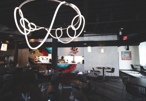 Modern restaurant interior featuring stylish lighting, minimalist decor, and a vibrant mural in the background.