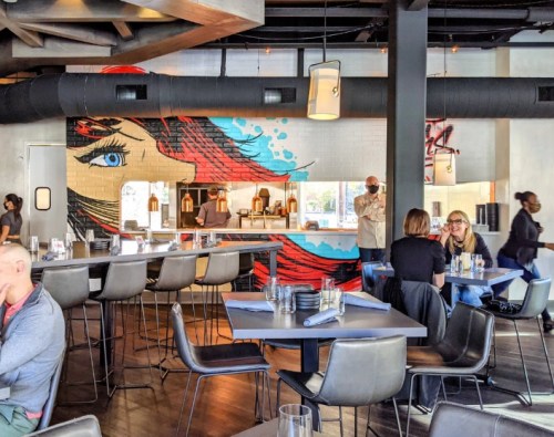 A modern restaurant interior featuring a colorful mural, sleek seating, and patrons dining at tables.