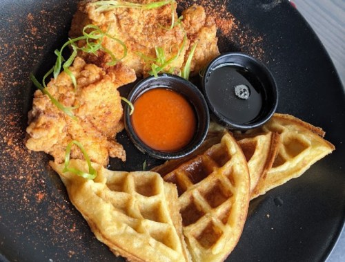 A plate featuring fried chicken, two waffles, and dipping sauces, garnished with green onions.