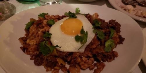 A plate of stir-fried rice topped with a sunny-side-up egg and garnished with fresh cilantro.