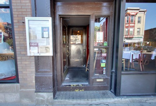 Entrance to a restaurant with wooden doors, menus displayed outside, and a view of the dining area through the windows.