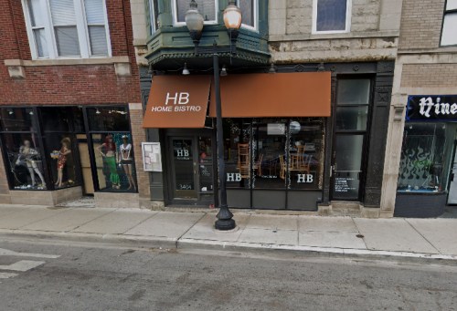 Exterior view of Home Bistro with an orange awning, flanked by shops, on a city street.