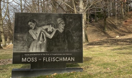 A large sign featuring a drawing of two figures, with the text "MOSS = FLEISCHMAN" in a park setting.