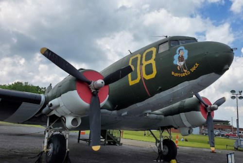 A vintage military aircraft, painted green with red propellers, featuring the name "Ruptured Duck" on its side.