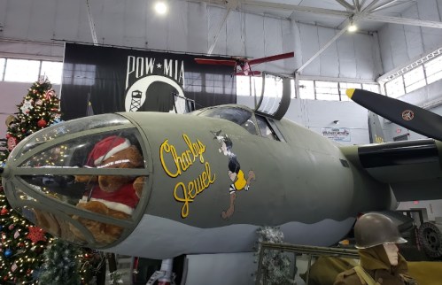 A vintage bomber aircraft displayed in a museum, decorated for the holidays with a Christmas tree nearby.