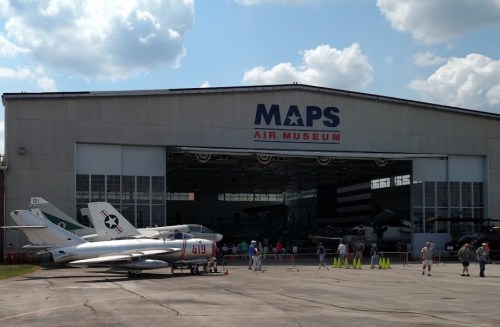 Exterior view of MAPS Air Museum with aircraft displayed outside and visitors gathered in front of the hangar.