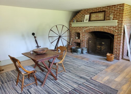 Cozy room with a wooden table, two chairs, a brick fireplace, and rustic decor on a woven rug.