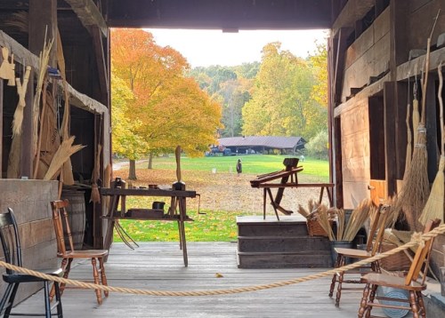 View from a rustic workshop, showcasing brooms and chairs, with vibrant autumn trees in the background.