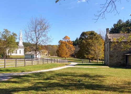 A scenic view of a rural landscape with a church, colorful trees, and a gravel path on a sunny day.