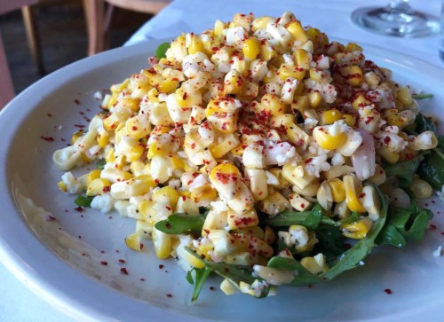 A plate of fresh corn salad topped with spices, served on a bed of arugula.