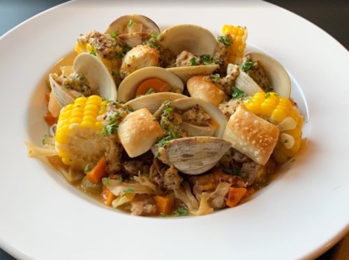 A bowl of pasta with clams, corn, and herbs, garnished with parsley and served in a creamy sauce.