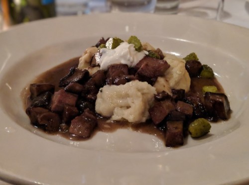 A plate of diced beef served over creamy mashed potatoes, garnished with green herbs and a dollop of sour cream.