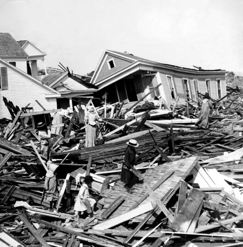Black and white photo of people navigating debris from destroyed buildings after a disaster.