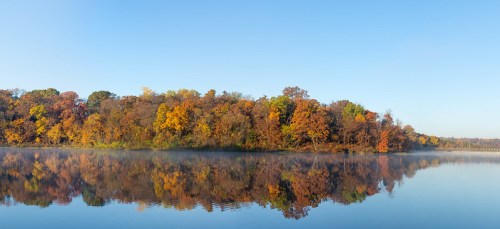 A serene lake reflecting vibrant autumn foliage under a clear blue sky.