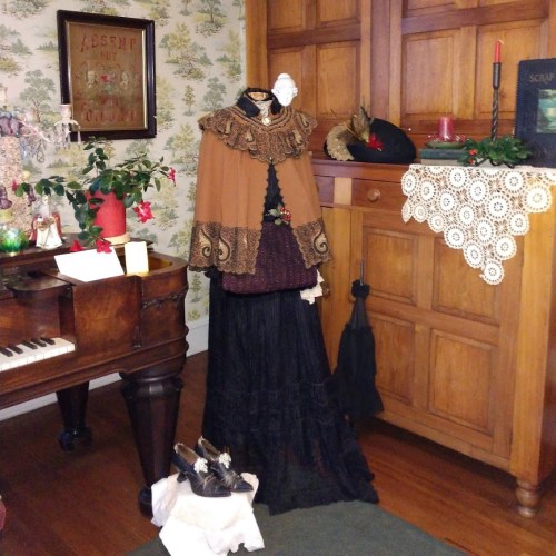 A vintage room with a piano, a dress on a mannequin, and decorative plants, showcasing a historical atmosphere.