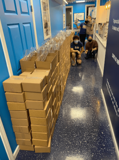 A hallway with stacked boxes and three people posing in masks, smiling in the background.