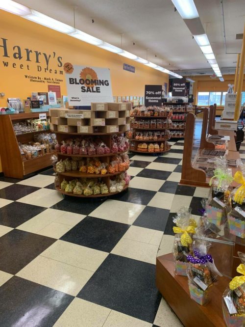 Interior of a candy store with checkered floors, featuring displays of colorful sweets and a "Blooming Sale" sign.