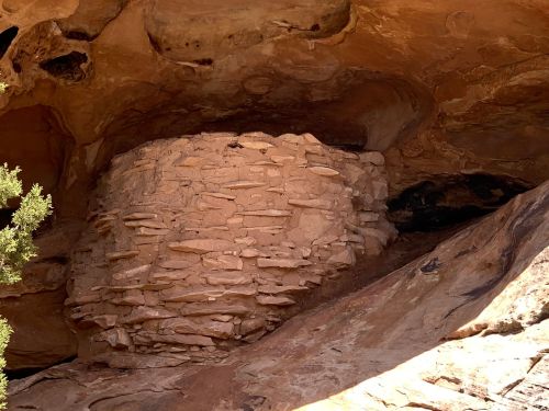 Ancient stone structure nestled in a rocky alcove, surrounded by natural formations and vegetation.