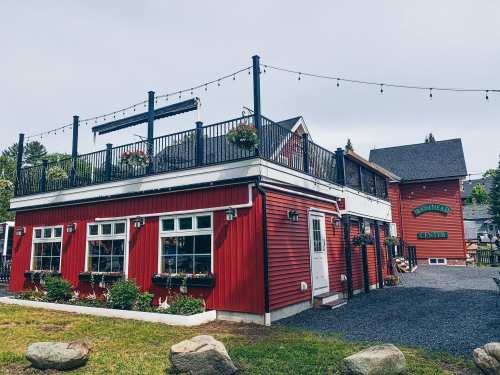 A red building with a rooftop patio, surrounded by greenery and gravel, featuring flower boxes on the windows.