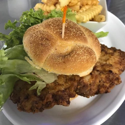 A plate with a crispy chicken sandwich, lettuce, and a side of curly fries.