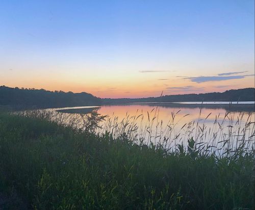A serene river at sunset, reflecting colorful skies and surrounded by lush greenery.