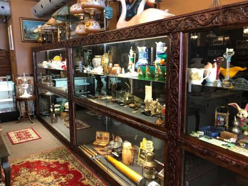 A display case filled with various antiques and collectibles in a vintage shop, with a patterned rug on the floor.