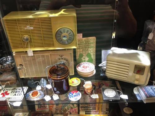 A display case filled with vintage radios, a jar, a clock, and various retro items.